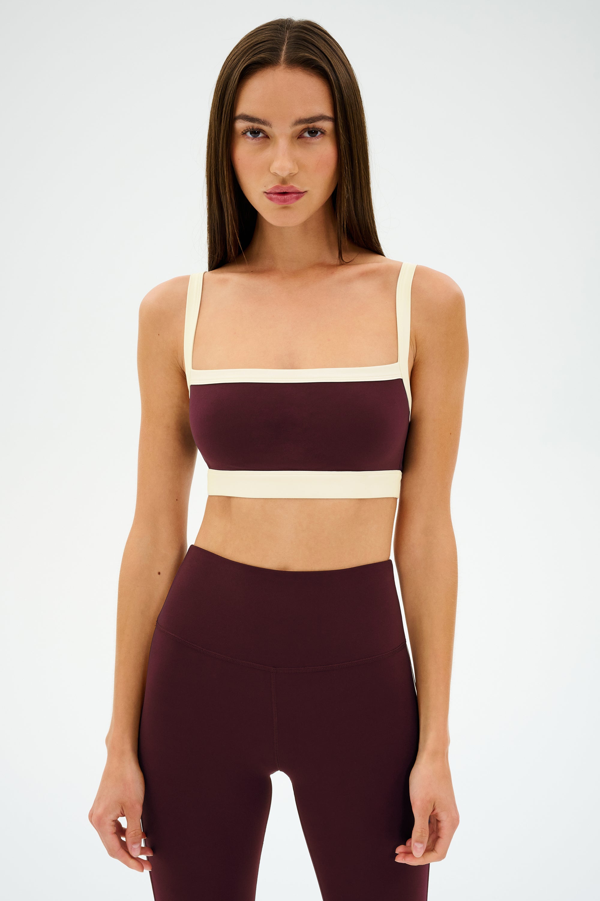 A woman faces forward against a white background, wearing the SPLITS59 Monah Rigor Bra in Dark Cherry/Creme with matching high-waisted leggings.