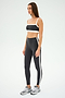 Someone wearing a black and white sports outfit featuring SPLITS59's Clare High Waist Rigor 7/8 leggings in Graphite/White and silver sneakers, ideal for gym workouts, stands confidently on a white background.
