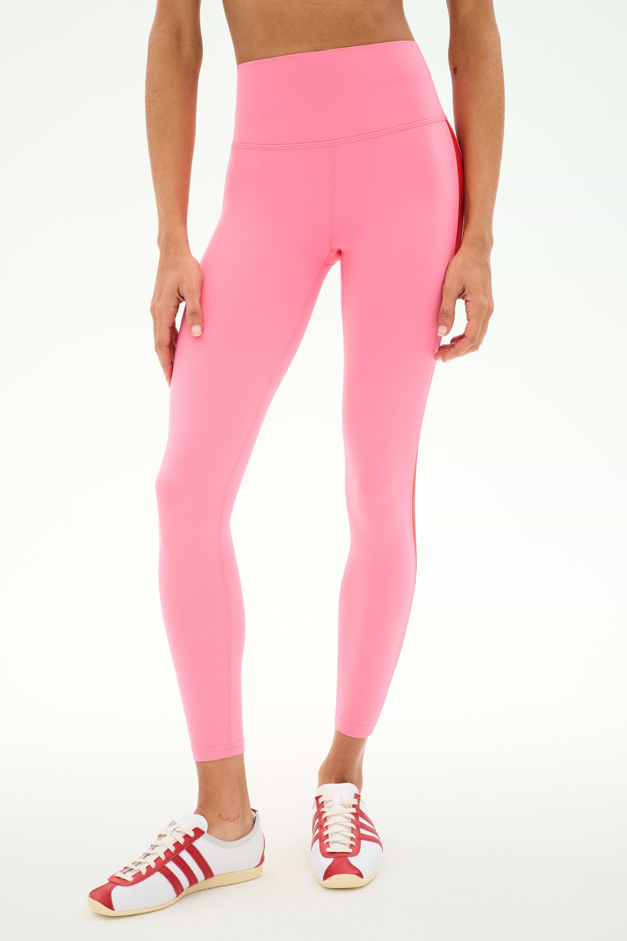 Wearing SPLITS59 Clare High Waist Rigor 7/8 leggings in Strawberry/Lotus Red, paired with red-and-white sneakers and set against a plain white background—ideal for stylish gym sessions.