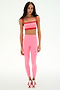 Wearing a SPLITS59 Monah Rigor Bra in Strawberry/Lotus Red, matching high-waisted leggings, and red-and-white sneakers, the person stands against a plain white background.