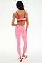A person stands facing away, wearing a SPLITS59 Monah Rigor Bra in Strawberry/Lotus Red, high-waisted pink leggings, and red-and-white athletic shoes against a plain white background.