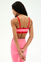 A woman stands with her back to the camera, wearing the SPLITS59 Monah Rigor Bra in Strawberry/Lotus Red and matching pink leggings, hands clasped behind her back.