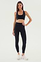 A woman stands against a plain background wearing the SPLITS59 Airweight High Waist Legging in black, paired with a black sports bra and white athletic shoes—an ideal look for hot yoga.