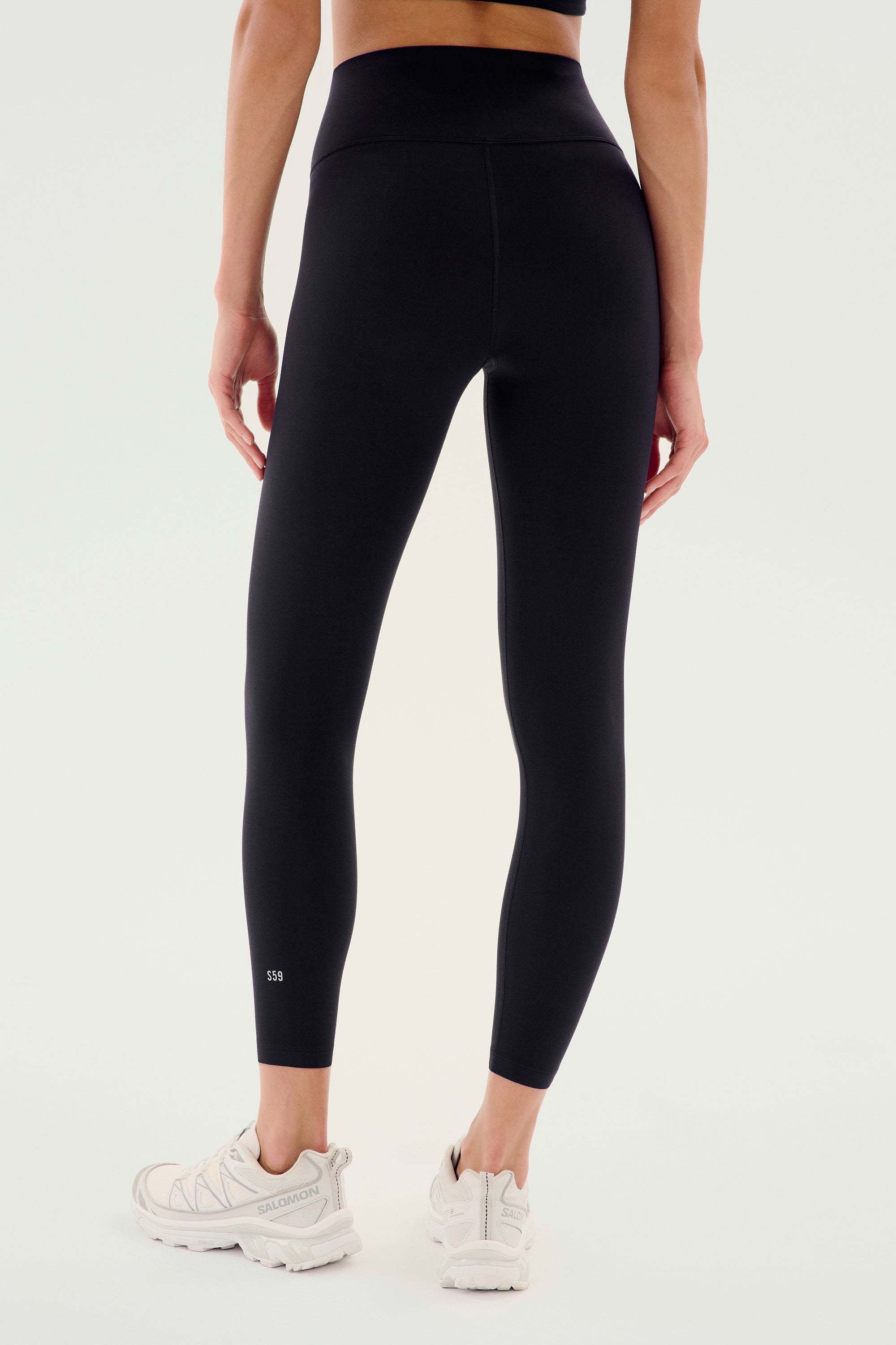A person wearing SPLITS59 Airweight High Waist Legging in Black and white sneakers stands with their back to a plain background. Soft Airweight fabric makes them perfect for hot yoga or everyday comfort.