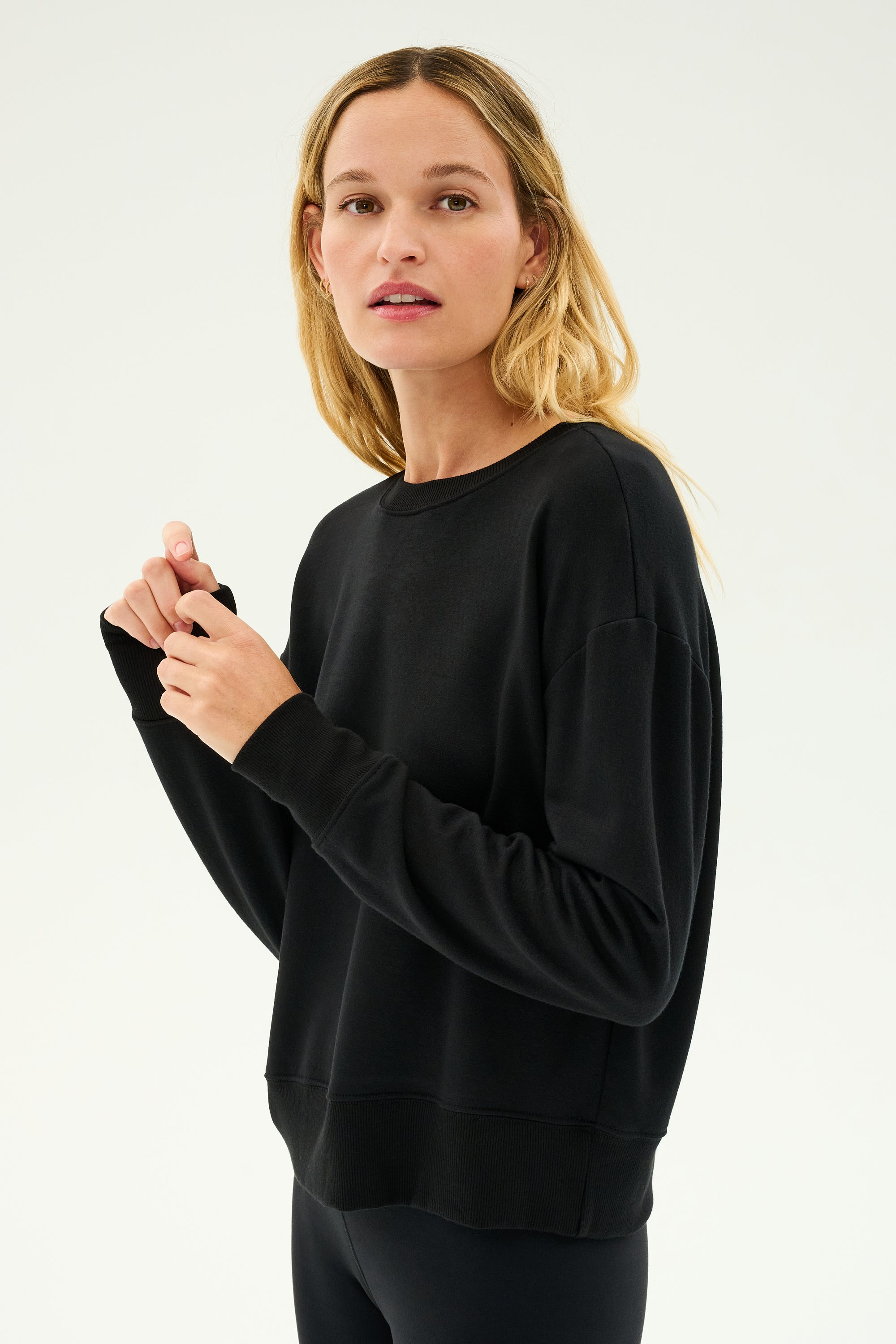 A person is wearing the SPLITS59 Sonja Fleece Sweatshirt in black, paired with black pants against a plain white background.