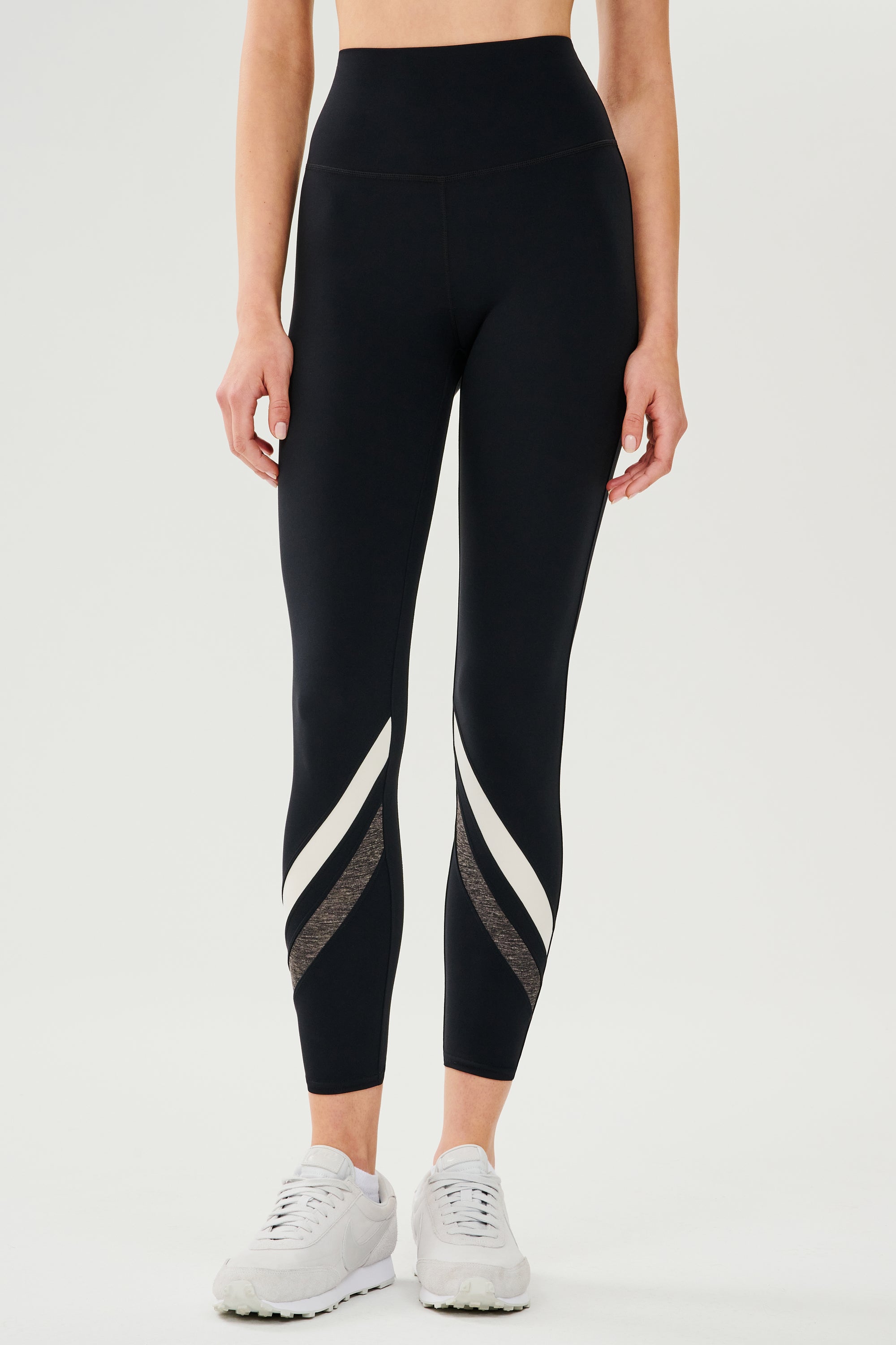Front view of girl wearing black leggings with two white and grey stripes across the shin with white shoes
