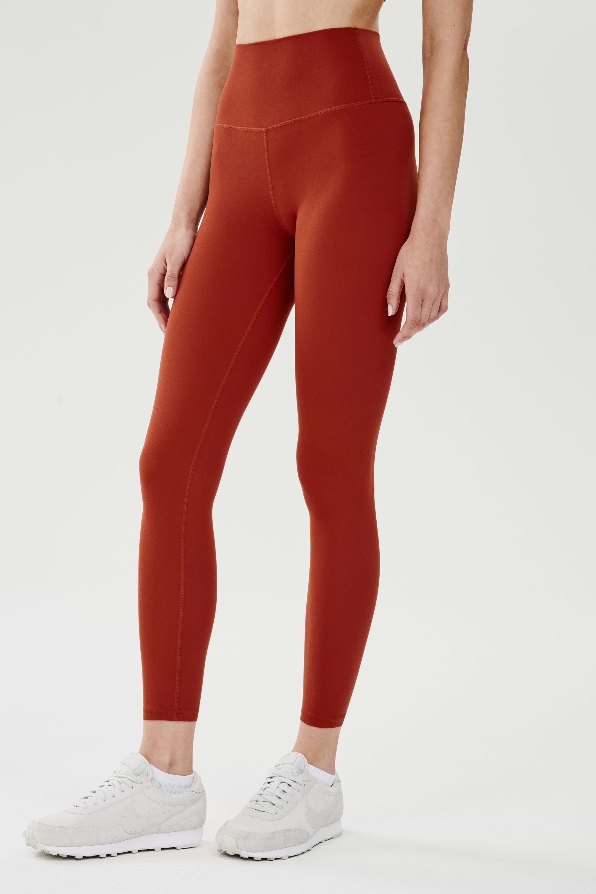 Side view of girl wearing highwasited dark orange leggings with white shoes