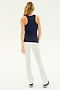 A person with long hair is standing, facing away from the camera. They are wearing the Kiki Rib Tank Full Length - Indigo from SPLITS59, white pants, and black and white sneakers—perfect attire for yoga or gym workouts. The background is plain and light-colored.