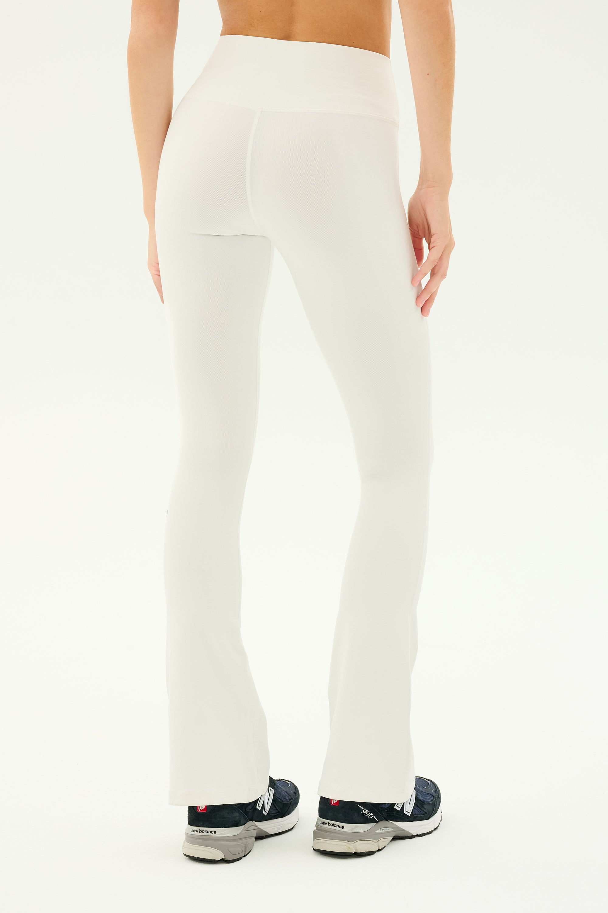Person shown from the back wearing SPLITS59 Raquel High Waist Flared Legging in white, made of 4-way stretch supposlex fabric, and black sneakers against a plain background.