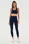 A woman stands facing forward, wearing an indigo Airweight High Waist Legging from SPLITS59 and a matching navy blue sports bra made from ultra luxe Airweight fabric, paired with white athletic shoes, against a plain light-colored background. Perfect for hot yoga sessions.