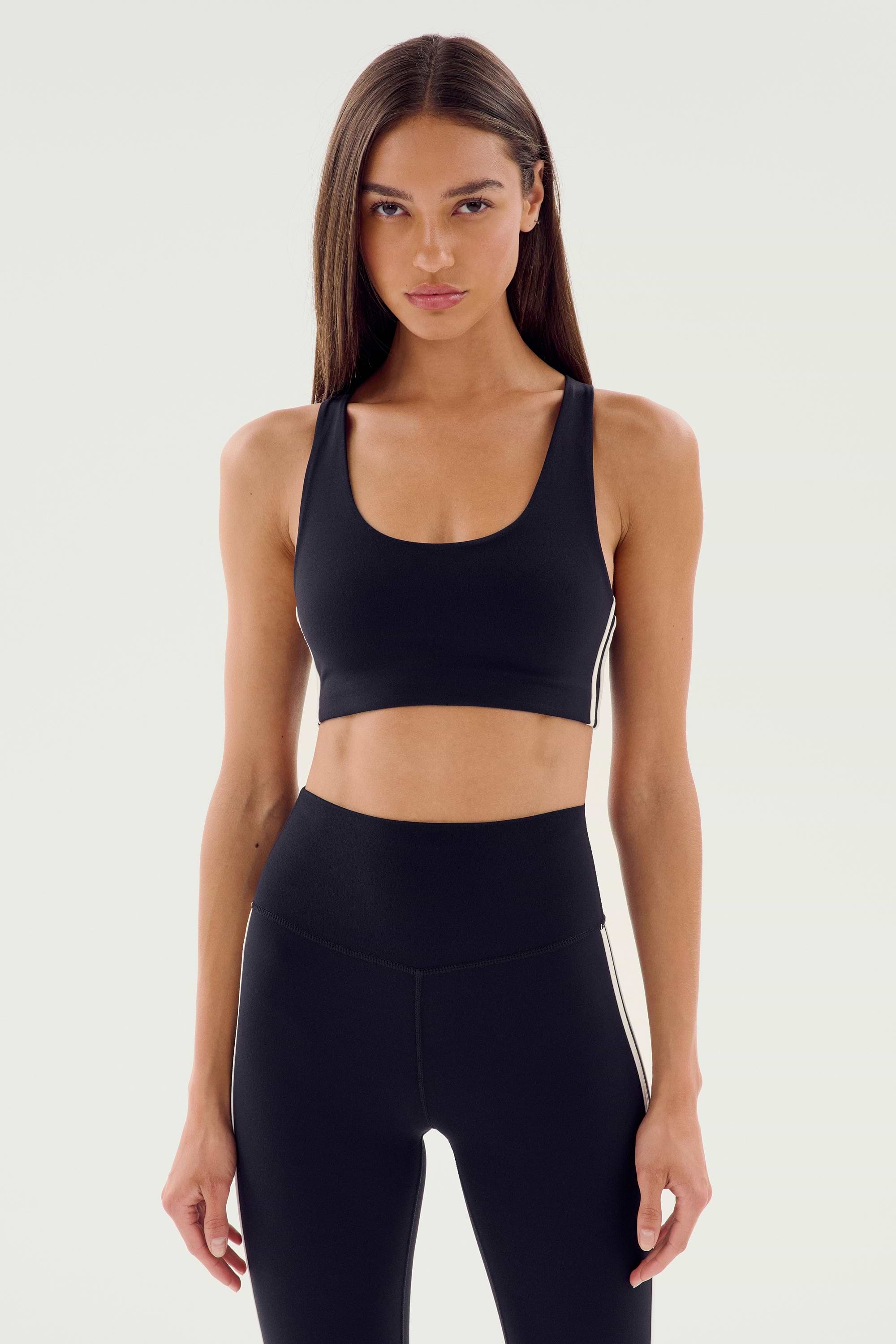 Person wearing a black Ella Airweight Bra by SPLITS59 and black high-waisted leggings, standing with arms relaxed by their sides.