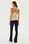 A woman is standing, facing away, wearing the SPLITS59 Loren Seamless Waist Length Tank in Nude, black pants, and white sneakers.