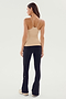 A woman is standing, facing away, wearing the SPLITS59 Loren Seamless Waist Length Tank in Nude, black pants, and white sneakers.