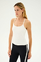 A woman with long blonde hair wearing the Airweight Tank in white by SPLITS59 and black leggings with a white stripe, perfect for hot yoga, stands against a plain background.