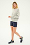 A person stands against a plain background, wearing a Sonja Fleece Sweatshirt in Heather Grey from SPLITS59, navy blue shorts, and navy blue sneakers.
