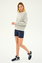 A person stands against a plain background, wearing a Sonja Fleece Sweatshirt in Heather Grey from SPLITS59, navy blue shorts, and navy blue sneakers.