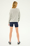 Person standing with their back to the camera, wearing a Sonja Fleece Sweatshirt in Heather Grey by SPLITS59, navy blue shorts, and sneakers, against a plain light background.