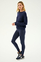 A person stands in profile against a plain light background, wearing the SPLITS59 Sonja Fleece Sweatshirt in Indigo, matching leggings, and black athletic shoes.