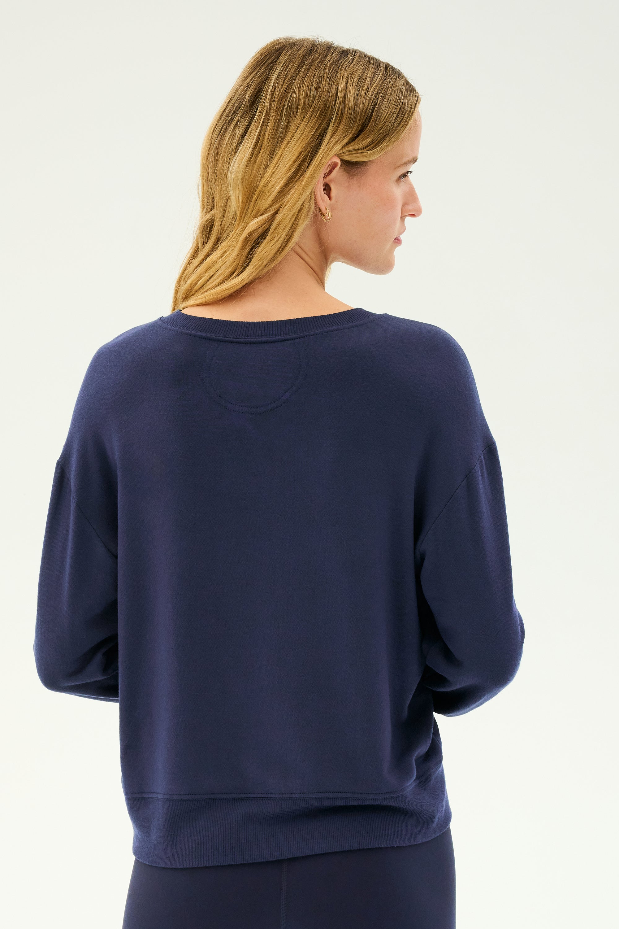 A woman with blond hair, seen from behind, wears the SPLITS59 Sonja Fleece Sweatshirt in Indigo—a loose-fitting, long-sleeve crewneck made in Los Angeles—against a plain light background.