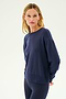 A person with long blond hair wears the SPLITS59 Sonja Fleece Sweatshirt in Indigo, paired with matching pants, standing against a plain light background.