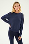 A woman stands against a plain background wearing the SPLITS59 Sonja Fleece Sweatshirt in indigo, paired with matching leggings and resting one hand on her hip.