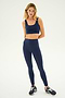 A woman is standing against a plain white background, modeling her Indigo Sprint Rigor Bra by SPLITS59, matching leggings, and black sneakers, ready for gym workouts and multi-sport performance.