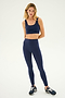 A woman wearing the SPLITS59 Sprint High Waist Rigor 7/8 leggings in Indigo with a matching navy blue sports bra and black and white athletic shoes stands against a plain white background.