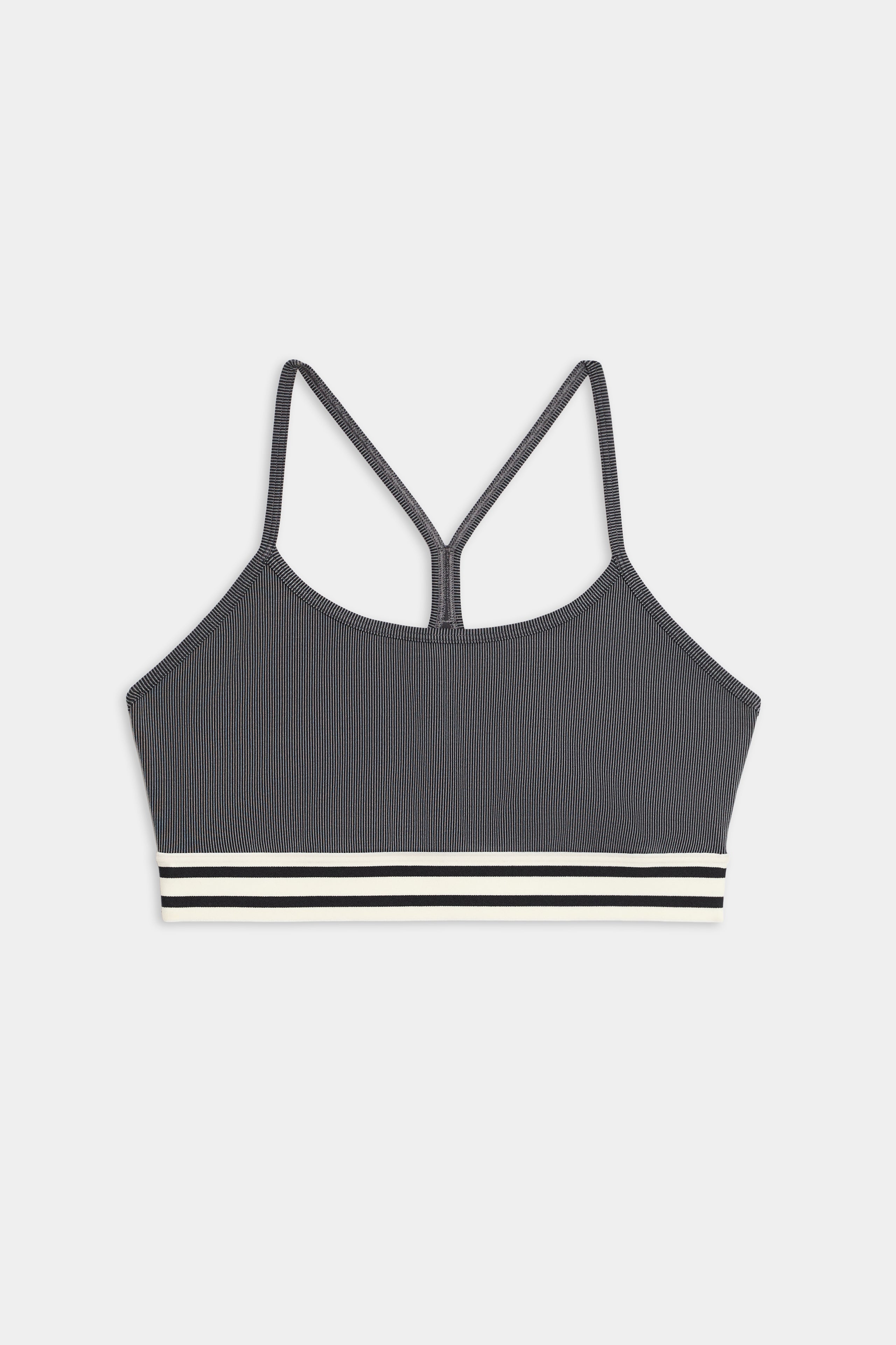 The Cali Active Rib Bra by SPLITS59 features a gray ribbed design, thin shoulder straps, a racerback, and a white-and-black striped elastic band at the bottom.