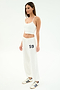 A woman in a white studio wears a white crop top and the SPLITS59 Andie Oversized Fleece Varsity 59 Sweatpant (White/59), ideal for cool weather workouts, finished with white sneakers with navy stripes.
