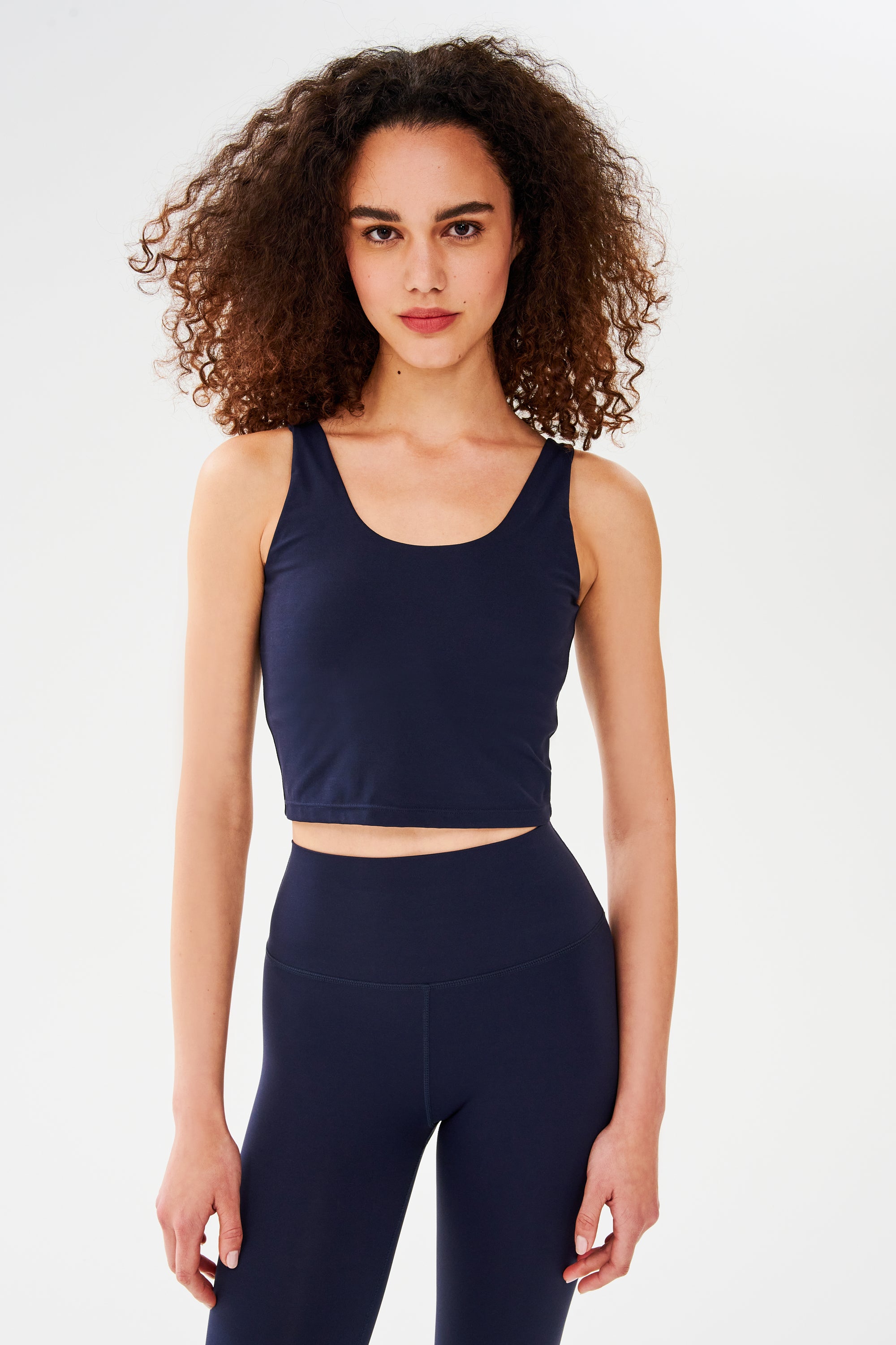 A person stands against a plain white background wearing the SPLITS59 Sprint Rigor Bralette in Indigo, looking directly at the camera—perfect for multi-sport performance.