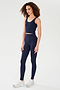 A person wears the SPLITS59 Sprint Rigor Bralette in Indigo with matching high-waisted leggings and white sneakers, standing against a plain white background, showcasing a multi-sport performance look.