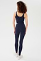 A person with curly hair wears the SPLITS59 Sprint Rigor Bralette in Indigo along with leggings and white sneakers, standing facing away on a plain white background.