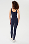 A person with curly hair wears the SPLITS59 Sprint Rigor Bralette in Indigo along with leggings and white sneakers, standing facing away on a plain white background.
