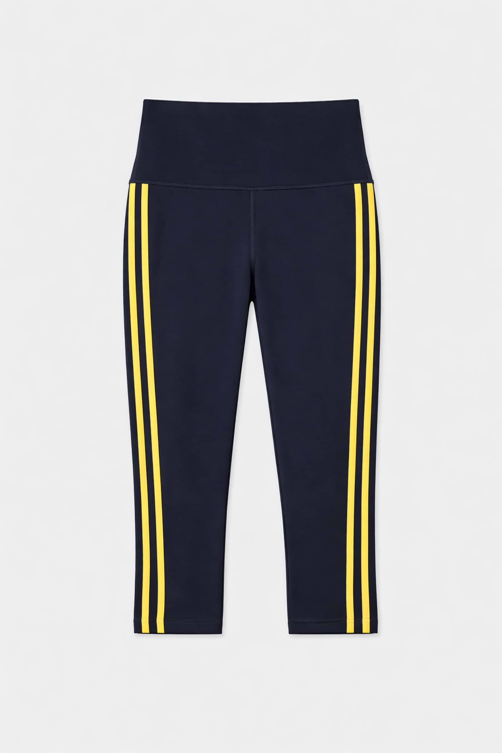 The SPLITS59 Ella High Waist Airweight Capri in Indigo/Bright Yellow features cropped leggings with two vertical yellow stripes on each side, displayed flat on a white background—ideal for hot yoga sessions.