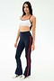 A woman wears the SPLITS59 Raquel High Waist Flared Legging in Indigo/Lotus Red, paired with a white sports bra and white sneakers, standing against a plain light background. The leggings offer 4-way stretch for comfort and performance.