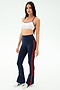 A woman wears the SPLITS59 Raquel High Waist Flared Legging in Indigo/Lotus Red, paired with a white sports bra and white sneakers, standing against a plain light background. The leggings offer 4-way stretch for comfort and performance.