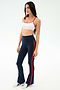 A woman poses in a studio wearing SPLITS59's Raquel High Waist Flared Legging in Indigo/Lotus Red and a white sports bra, paired with white sneakers against a plain background.