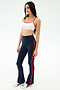 A woman poses in a studio wearing SPLITS59's Raquel High Waist Flared Legging in Indigo/Lotus Red and a white sports bra, paired with white sneakers against a plain background.