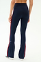 A person is seen from the back wearing SPLITS59's Raquel High Waist Flared Legging in Indigo/Lotus Red, featuring a high waist and red side stripes, set against a plain background.