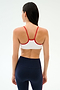 A woman with long dark hair, seen from behind, wears the SPLITS59 Loren Seamless Bra in White/Lotus Red and high-waisted navy leggings—ideal for yoga or gym—against a plain light background.