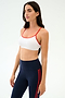 A woman wears the SPLITS59 Loren Seamless Bra in White/Lotus Red with navy high-waisted leggings featuring red stripes, perfect for gym workouts, set against a plain background.