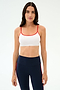 A woman faces forward in a SPLITS59 Loren Seamless Bra - White/Lotus Red, perfect for workouts, paired with high-waisted navy leggings featuring red side stripes, set against a plain light background.
