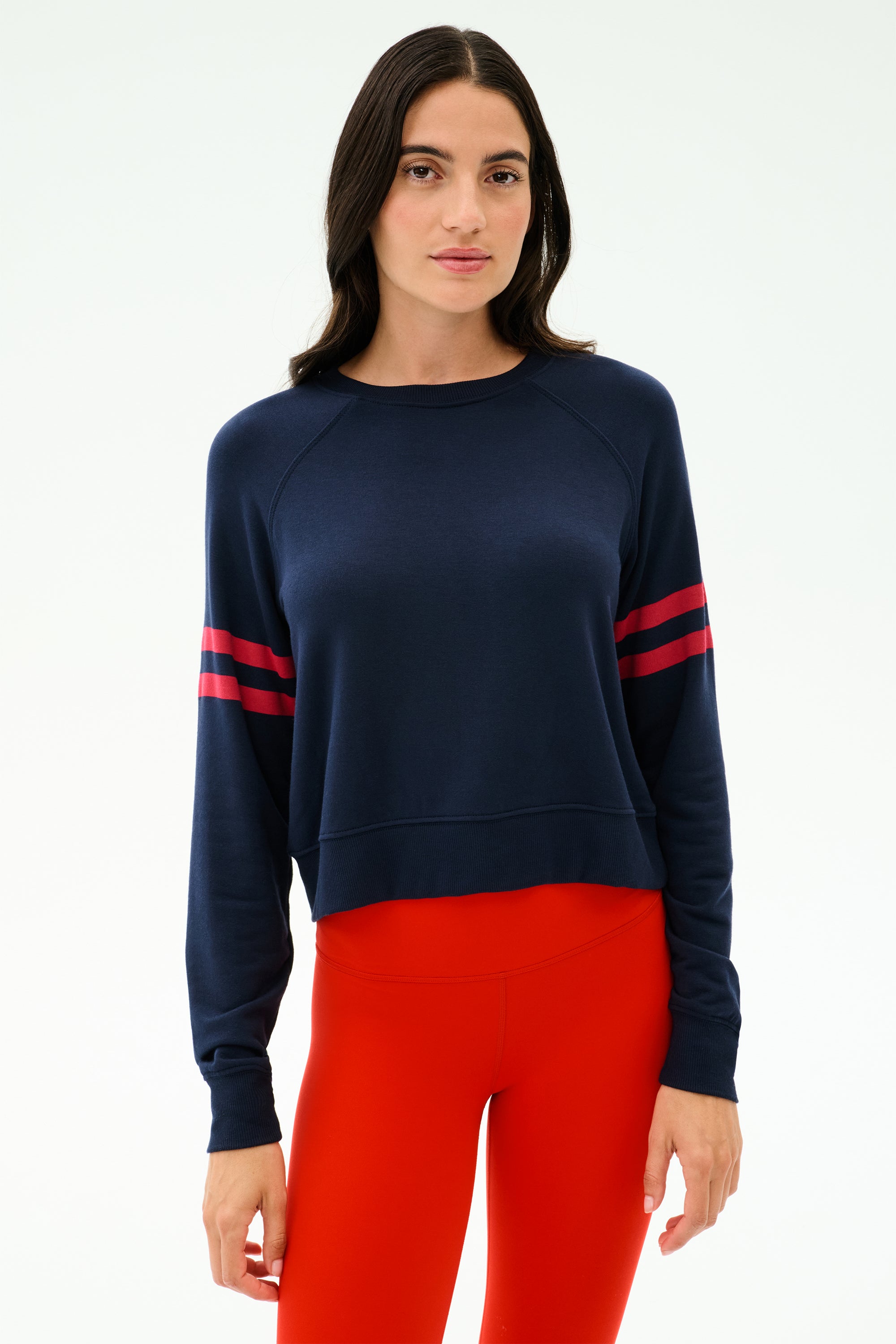 A woman faces forward wearing the SPLITS59 Brooks Stripe Fleece Sweatshirt in Indigo/Lotus Red and bright red leggings against a plain light background.