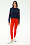 A woman stands against a plain background, wearing the SPLITS59 Brooks Stripe Fleece Sweatshirt in Indigo/Lotus Red, bright red leggings, and white sneakers.