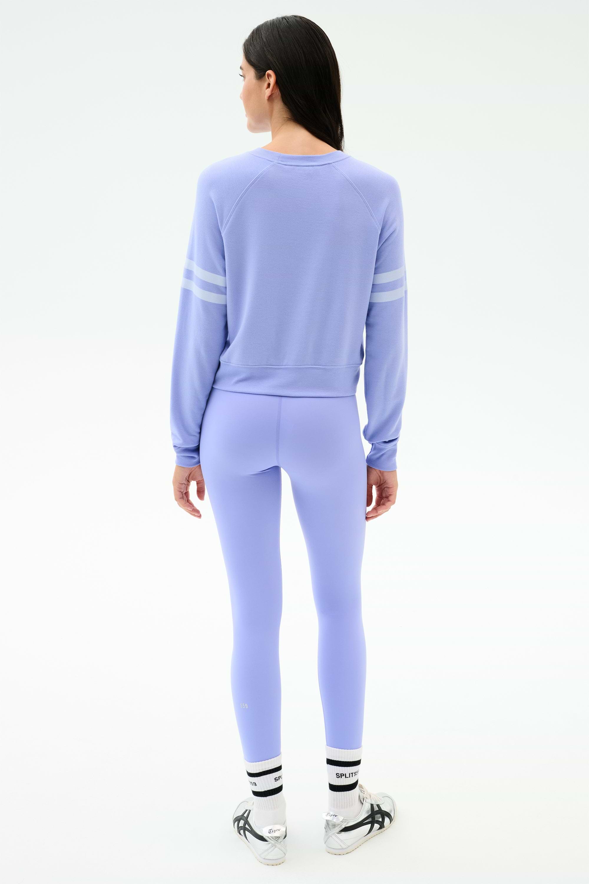 A person faces away, wearing the SPLITS59 Brooks Stripe Fleece Sweatshirt in Purple Haze/White and matching leggings made in Los Angeles, plus white socks with black text and gray sneakers, set against a plain white background.