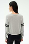 A woman with long dark hair stands with her back to the camera, wearing the SPLITS59 Brooks Stripe Fleece Sweatshirt in Heather Grey/Black and black leggings.