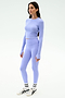 A woman stands against a white background wearing the SPLITS59 Louise Rib Long Sleeve Crop in Purple Haze, paired with matching leggings, white socks, and white sneakers.