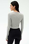 A woman with long dark hair in a braid stands with her back to the camera, wearing the SPLITS59 Louise Rib Long Sleeve Crop in Heather Grey and black leggings—perfect as a workout top—against a plain light background.