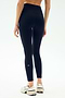 A person wearing SPLITS59 Sprint High Waist Rigor 7/8 leggings in Indigo and white sneakers stands with their back to the camera against a light background.