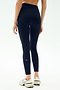 A person wearing SPLITS59 Sprint High Waist Rigor 7/8 leggings in Indigo and white sneakers stands with their back to the camera against a light background.